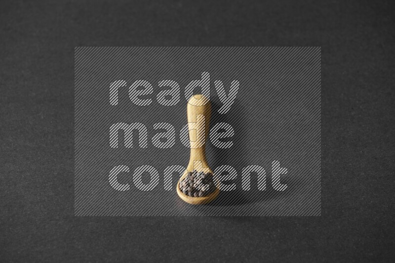 A wooden spoon full of black pepper on a black flooring