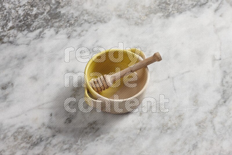 Multicolored pottery bowl with wooden honey dipper in it on grey marble background