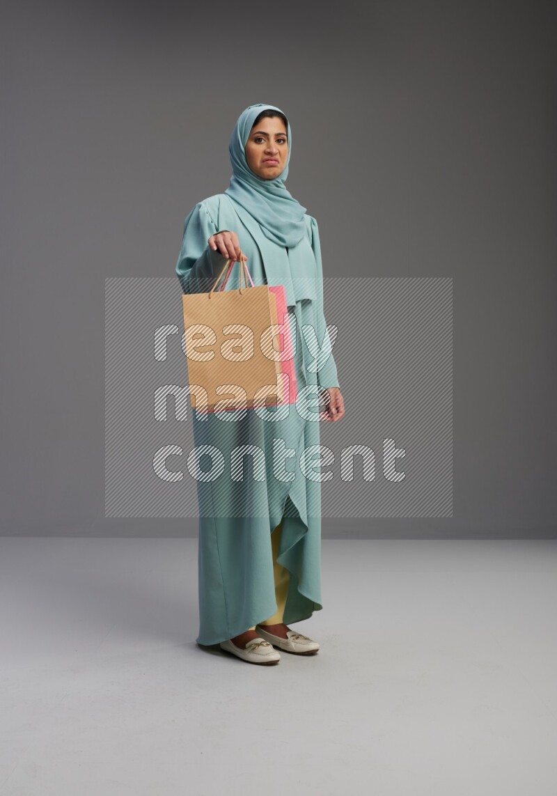 Saudi Woman wearing Abaya standing holding shopping bag on Gray background
