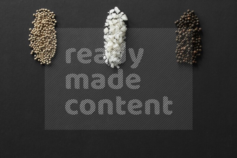 White pepper, salt and black pepper lined on a black background