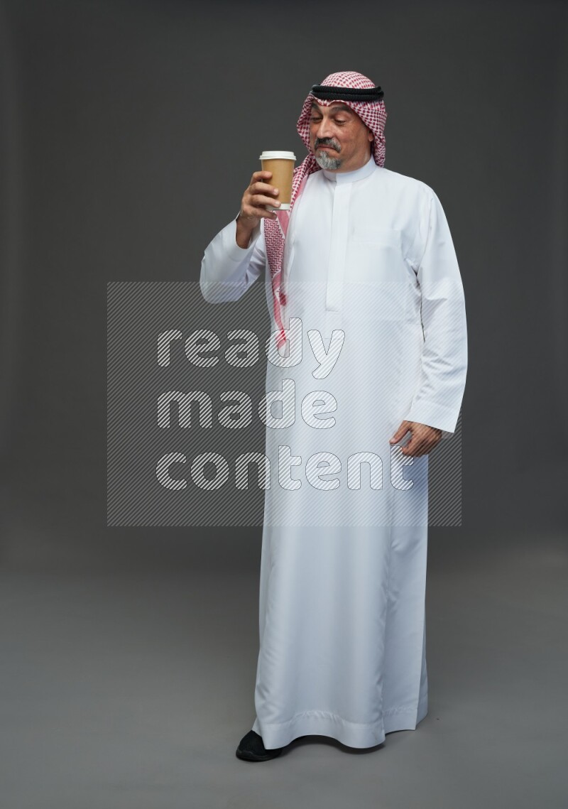 Saudi man with shomag Standing holding paper cup on gray background