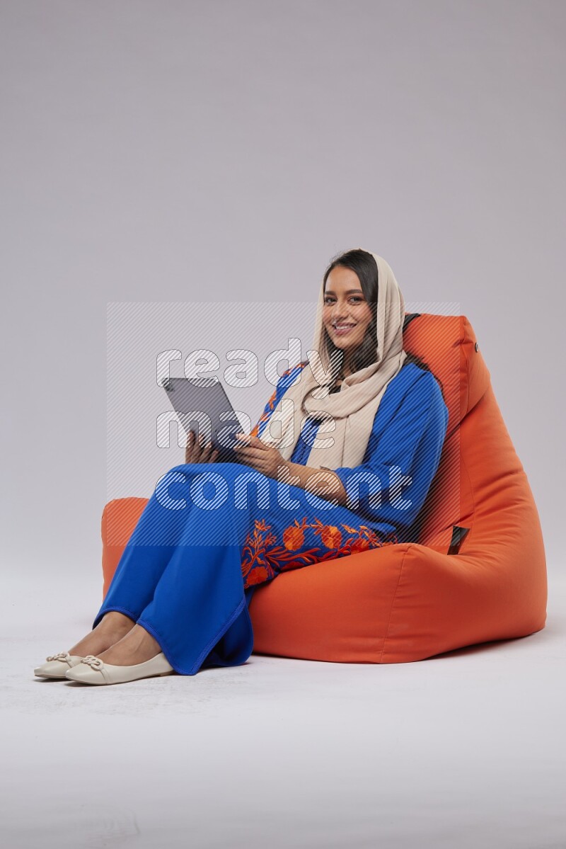 A Saudi woman sitting on an orange beanbag and working on tablet
