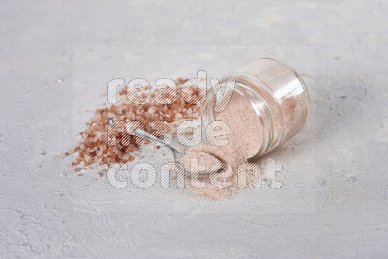 A glass jar full of fine himalayan salt with some himalayan crystals beside it on a white background