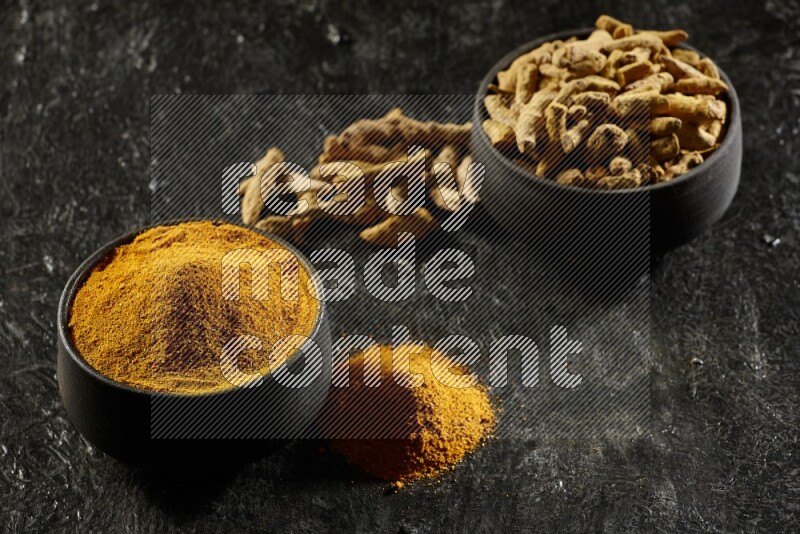 وعاءان من الفخار باللون الأسود، أحدهما ممتلئ ببودرة الكركم والآخر ممتلئ بأصابع كاملة من الكركم المجفف على خلفية سوداء