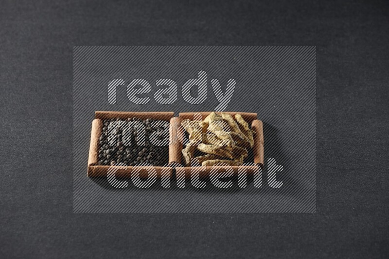 مربعان من أعواد القرفة ممتلئان بحبوب الفلفل الأسود وأصابع الكركم علي خلفية سوداء