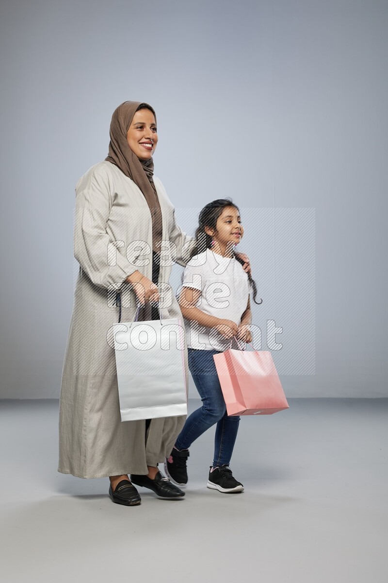 Mom and daughter holding shopping bags on gray background