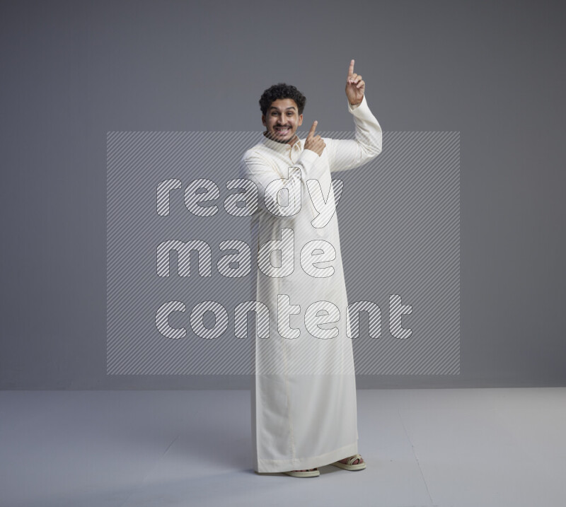 A Saudi man standing wearing thob interacting with the camera on gray background
