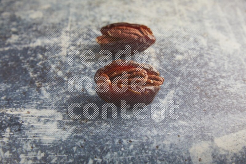 two pecan stuffed madjoul dates on a rustic blue background