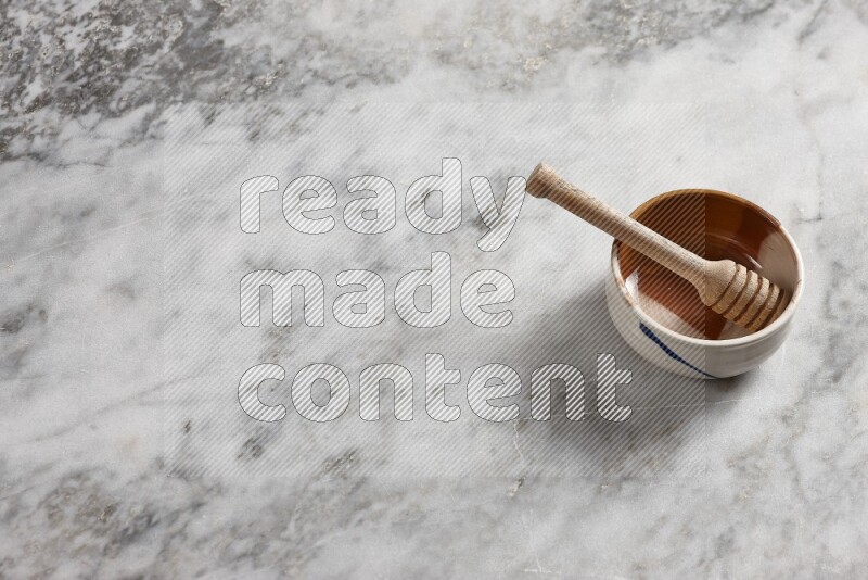 Multicolored pottery bowl with wooden honey dipper in it on grey marble background
