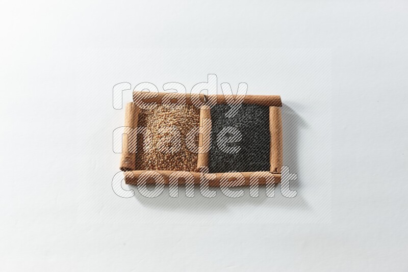 مربعان من أعواد القرفة ممتلئان بحبوب الخردل وحبة البركة السوداء علي خلفية بيضاء