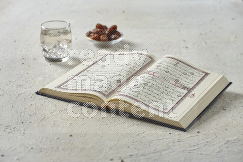 Quran with dates, prayer beads and different drinks all placed on textured white background