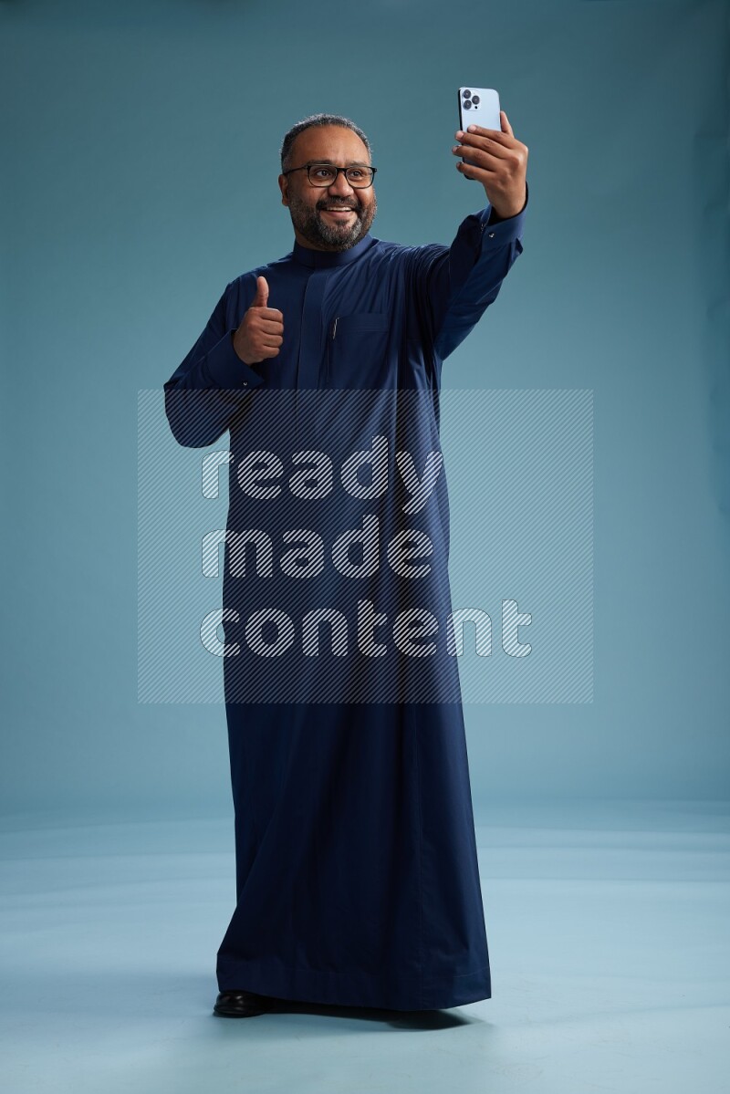 Saudi Man without shimag Standing taking selfie on blue background