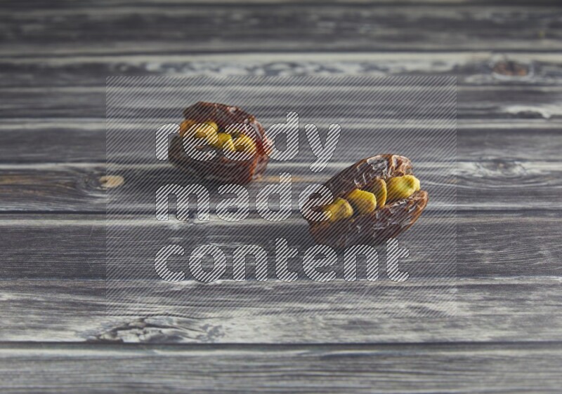 two pistachio stuffed madjoul dates on a wooden grey background