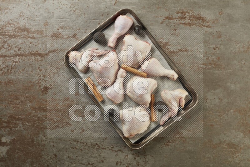 Mixed fresh chicken pieces in an oven tray on a textured rustic background