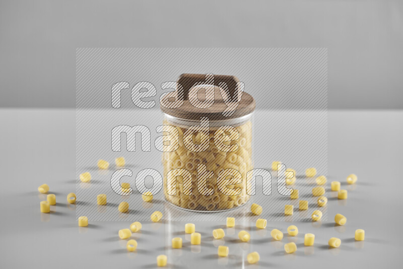 Raw pasta in a glass jar on light grey background