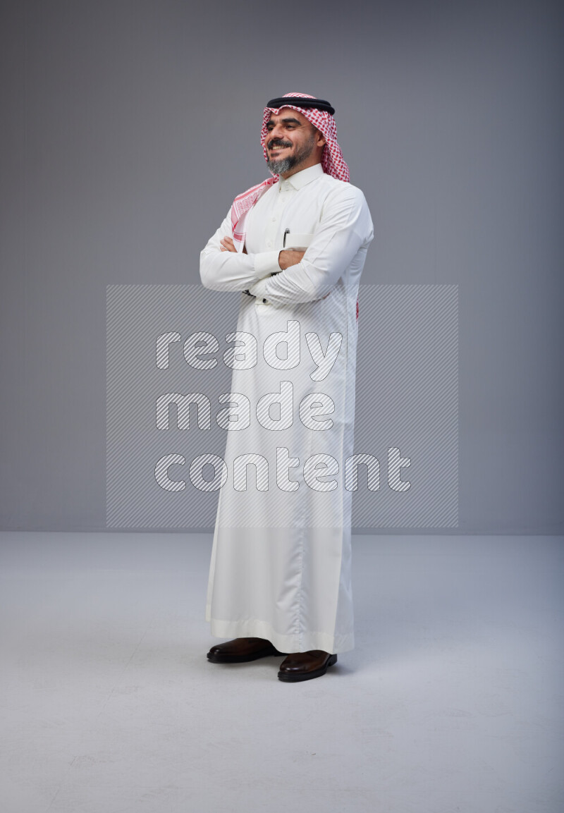 Saudi man Wearing Thob and red Shomag standing with crossed arms on Gray background
