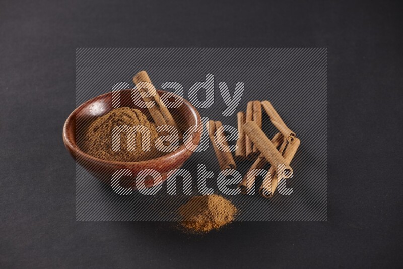 Cinnamon powder in a wooden bowl with a cinnamon sticks on black background