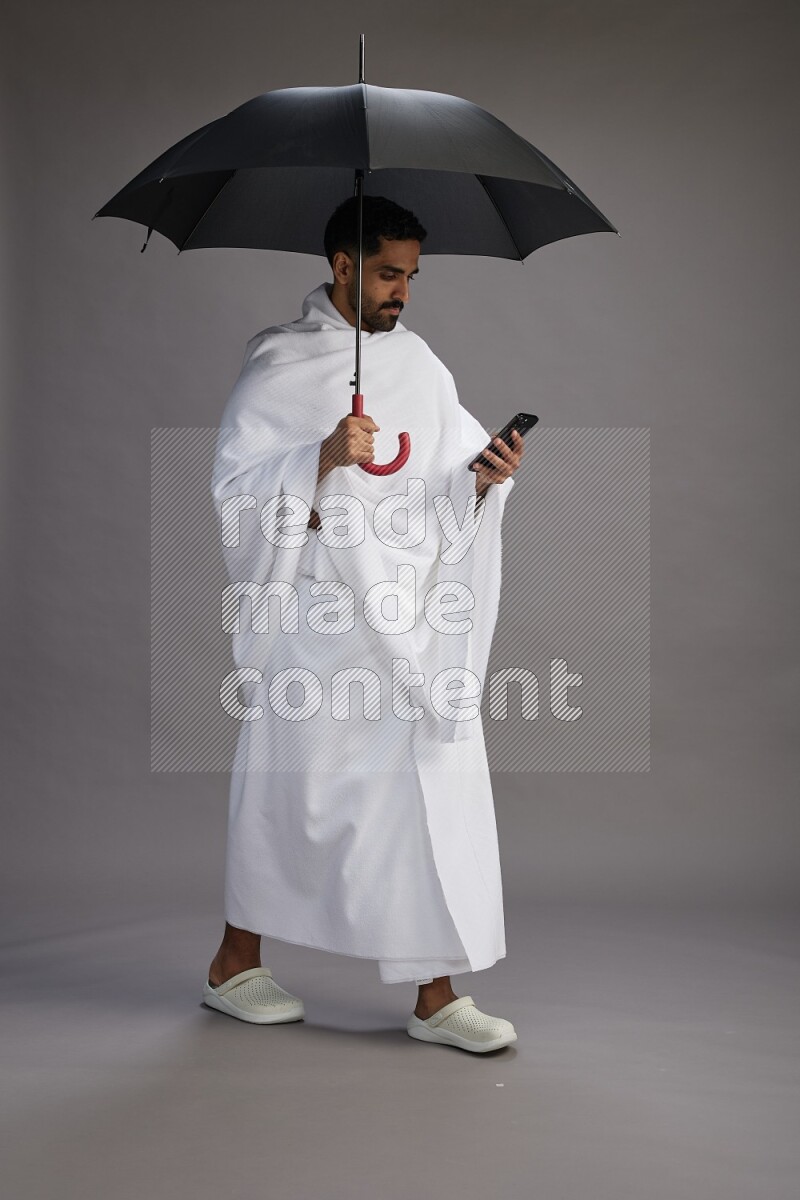 A man wearing Ehram Standing holding umbrella on gray background