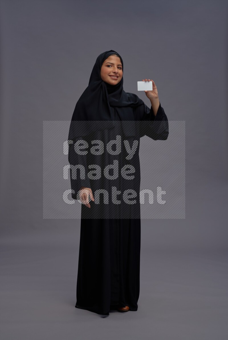 Saudi woman wearing Abaya standing holding ATM card on gray background