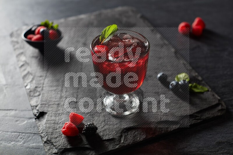 A glass of mixed berries juice with mint leaves on black background