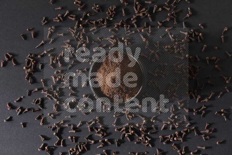 وعاء فخاري أسود ممتلئ ببودرة القرنفل وحبوب القرنفل على خلفية سوداء