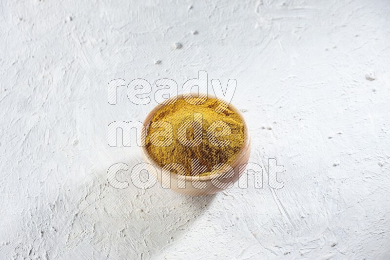 A wooden bowl full of turmeric powder on a textured white flooring