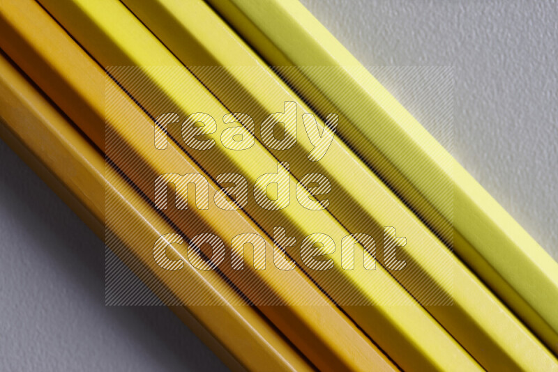A collection of sharpened colored pencils arranged showcasing a gradient of yellow hues on grey background