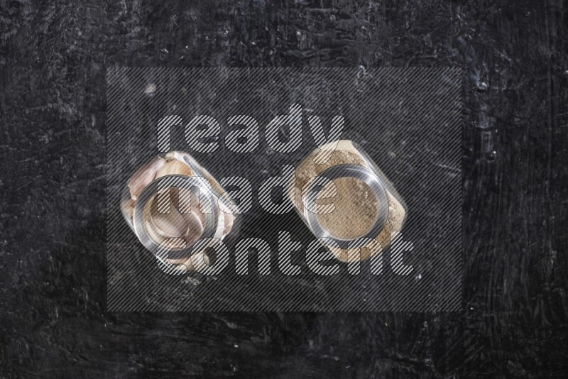 2 glass spice jars full of garlic powder and cloves on a textured black flooring