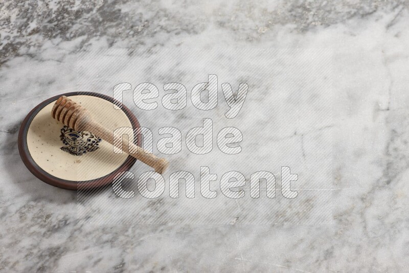 Decorative pottery plate with wooden honey dipper in it on grey marble background