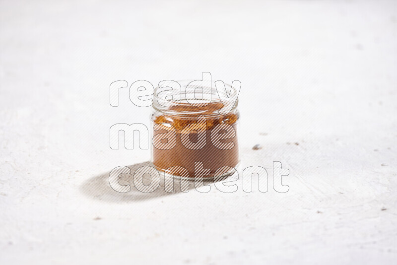A glass jar full of ground paprika powder on white background