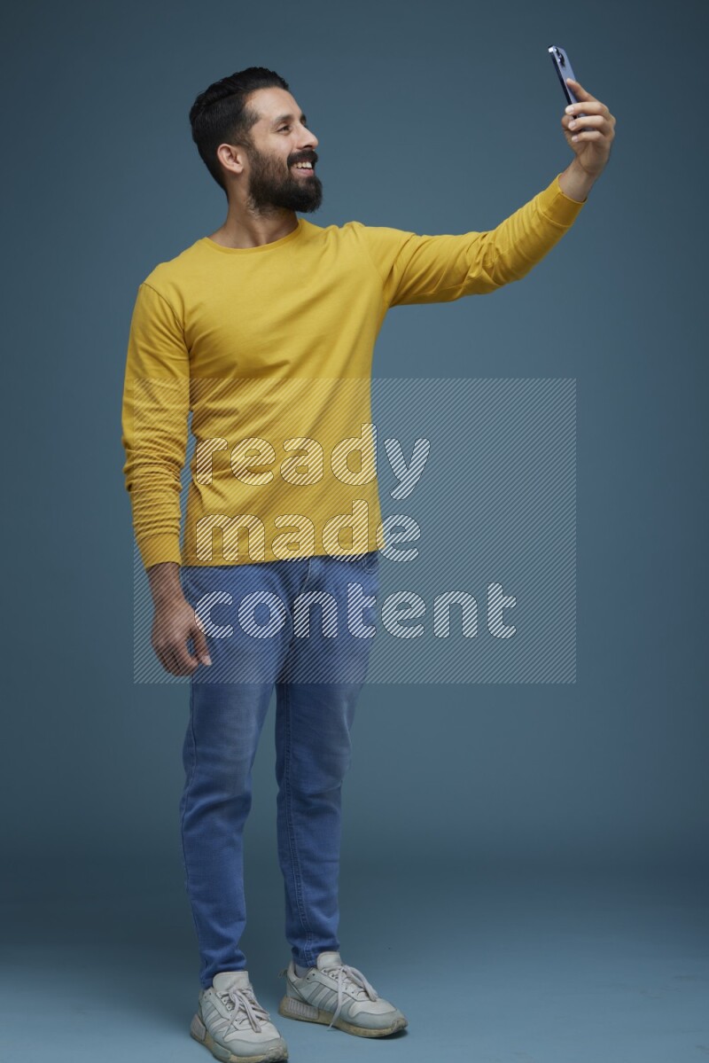 Man Taking a Selfie  in a blue background wearing a yellow shirt