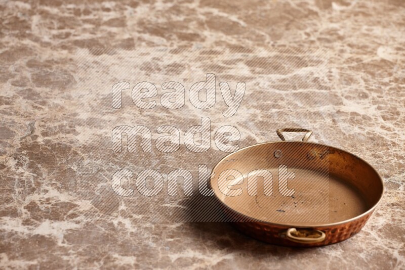 A small copper pan on beige marble background