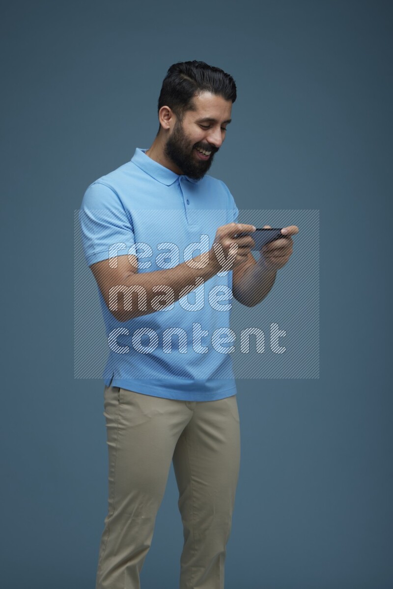 Man playing a game on his phone in a blue background wearing a Blue shirt