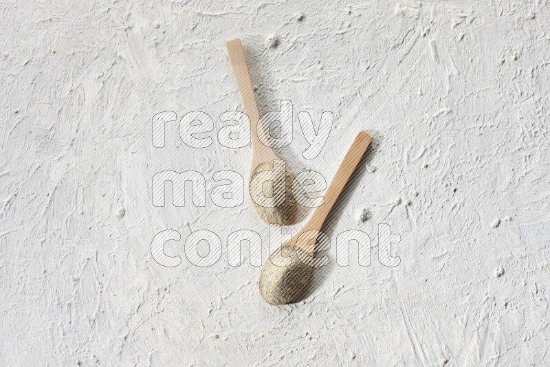 2 wooden spoons full of white pepper powder on textured white flooring