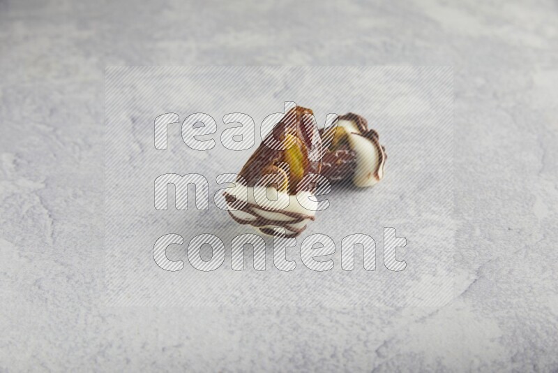 two pistachio stuffed dates covered with white chocolate with dark chocolate drizzle on a light grey background