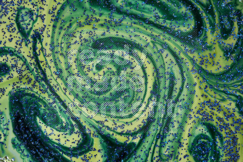 A close-up of sparkling blue glitter scattered on swirling blue and green background