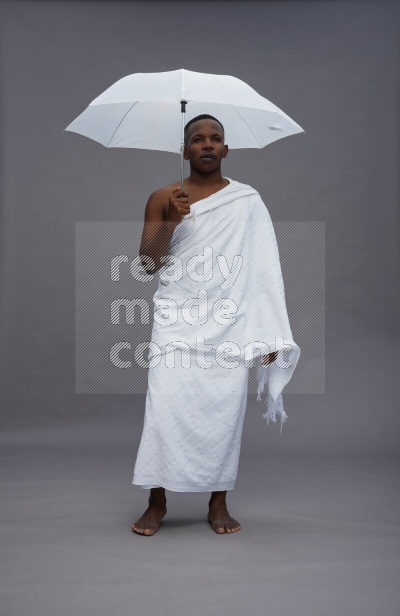 A man wearing Ehram Standing holding umbrella on gray background