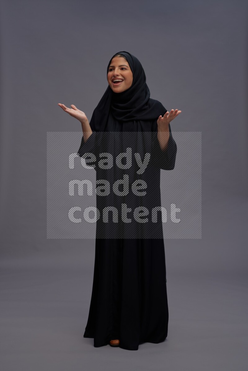 Saudi woman wearing Abaya standing interacting with the camera on gray background