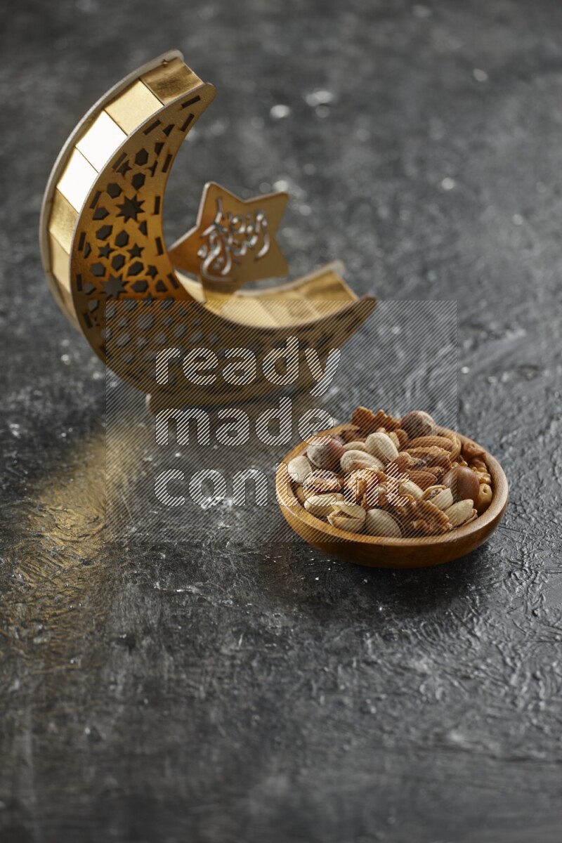 A wooden golden crescent lantern with different drinks, dates, nuts, prayer beads and quran on textured black background