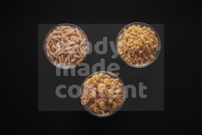 Different pasta types in glass bowls on black background