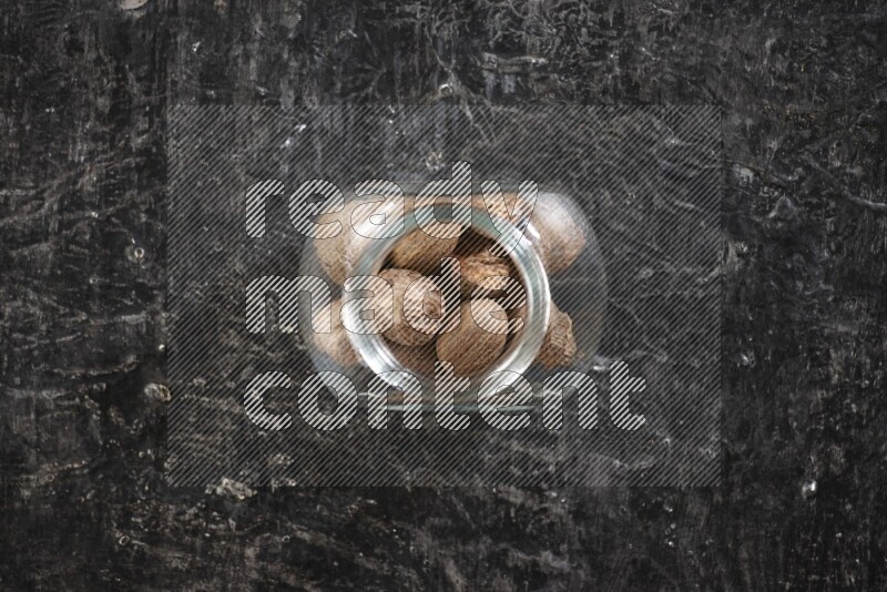 وعاء زجاجي ممتلئ بحبوب جوزة الطيب الكاملة علي خلفية سوداء