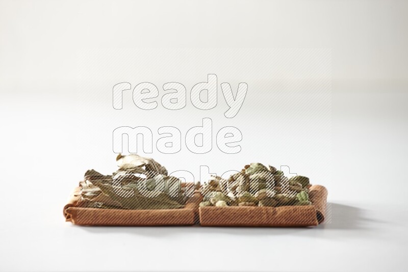 مربعان من أعواد القرفة ممتلئان بحبوب الهيل وأوراق الغار علي خلفية بيضاء