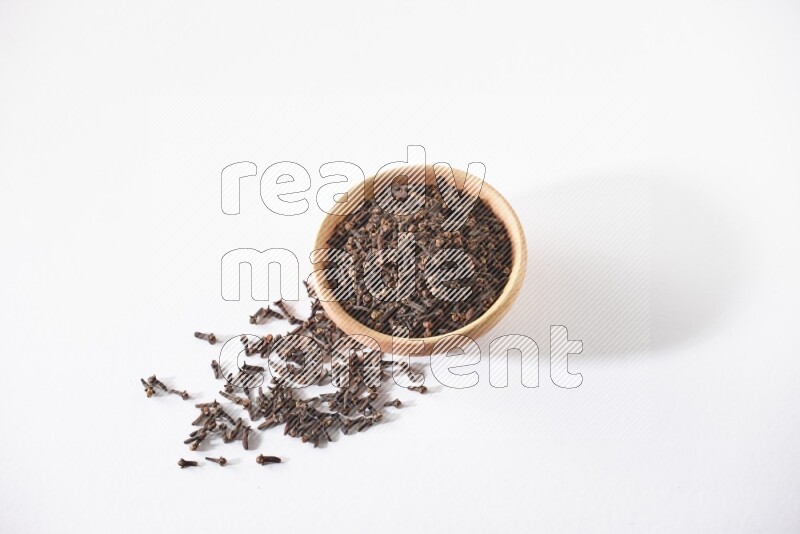 وعاء خشبي ممتلئ بالقرنفل مع حبوب متناثرة على أرضية بيضاء