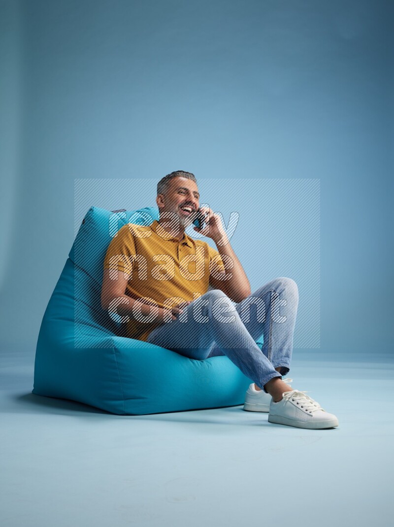 A man sitting on a blue beanbag and talking on the phone