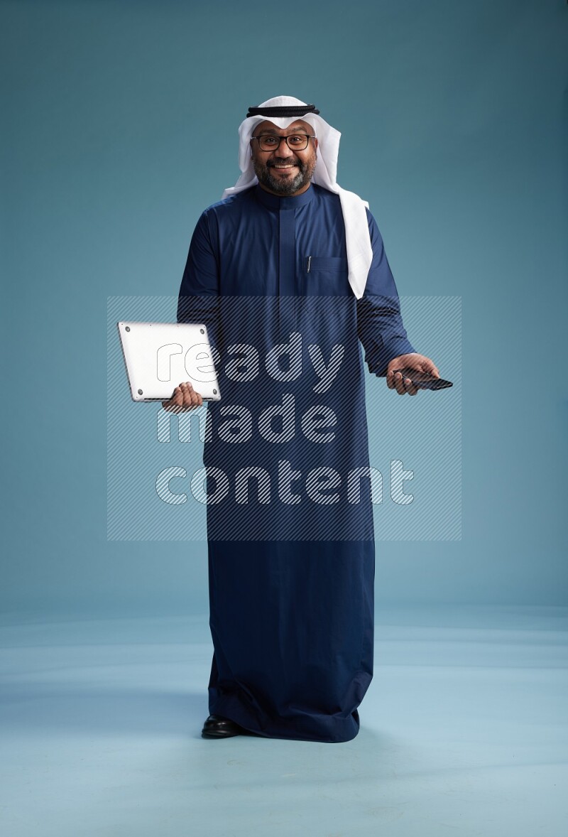 Saudi Man with shimag Standing texting on phone on blue background