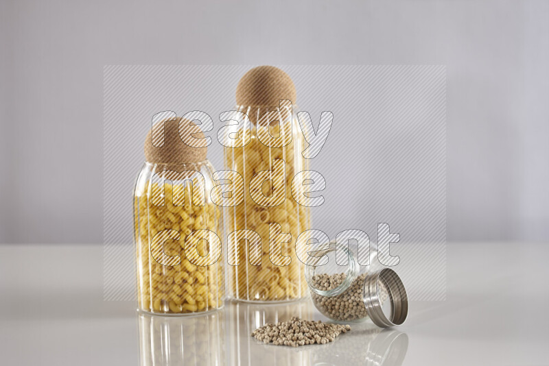 Raw pasta in glass jars with white peppers on light grey background