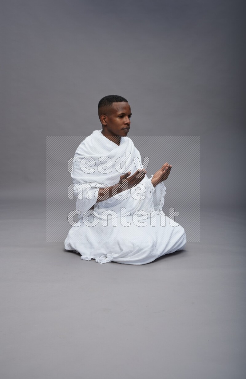 A man wearing Ehram sitting on floor dua'a on gray background