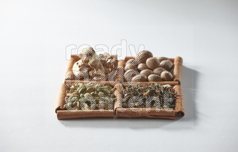 4 مربعات من أعواد القرفة ممتلئة بجوزة الطيب والزنجبيل المجفف والهيل والريحان المجفف على أرضية بيضاء