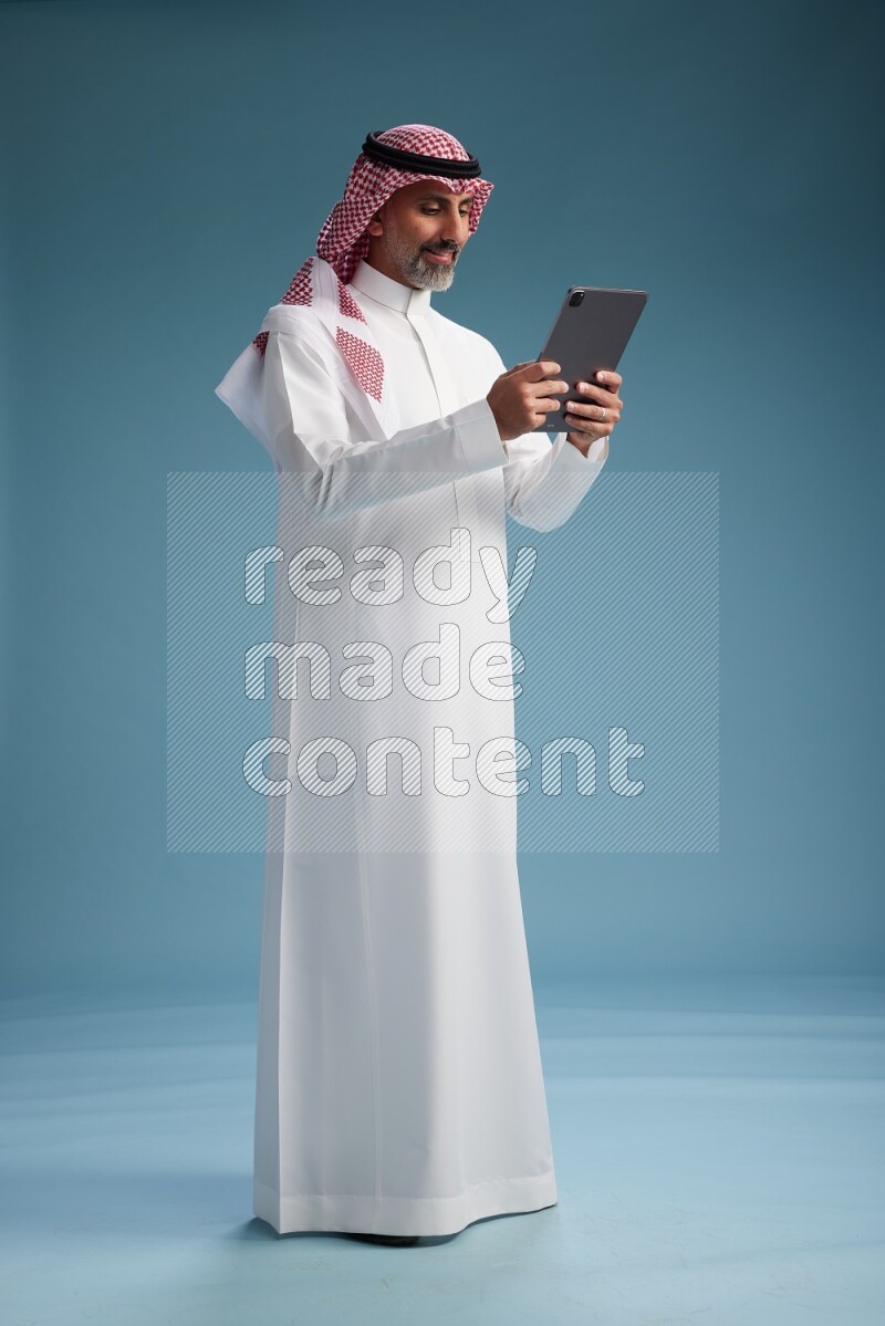 Saudi man wearing thob and shomagh with tablet on Blue background
