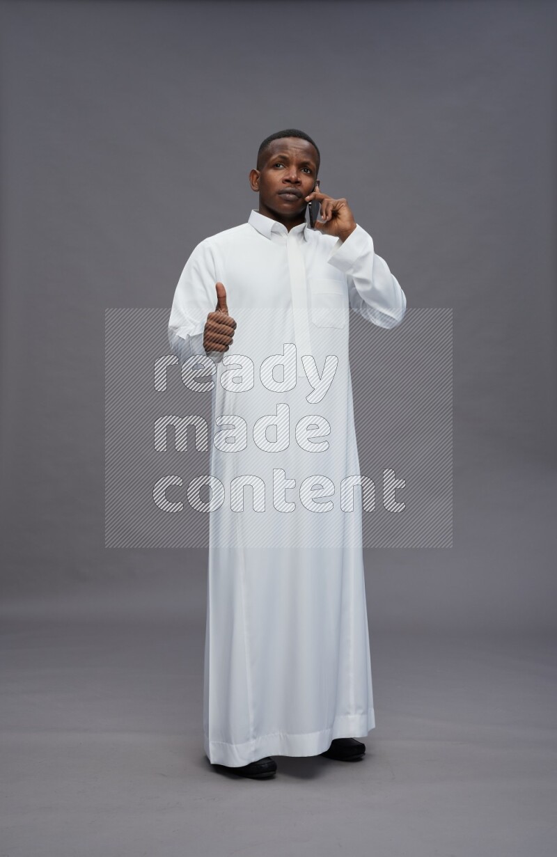 Saudi man wearing thob standing talking on phone on gray background
